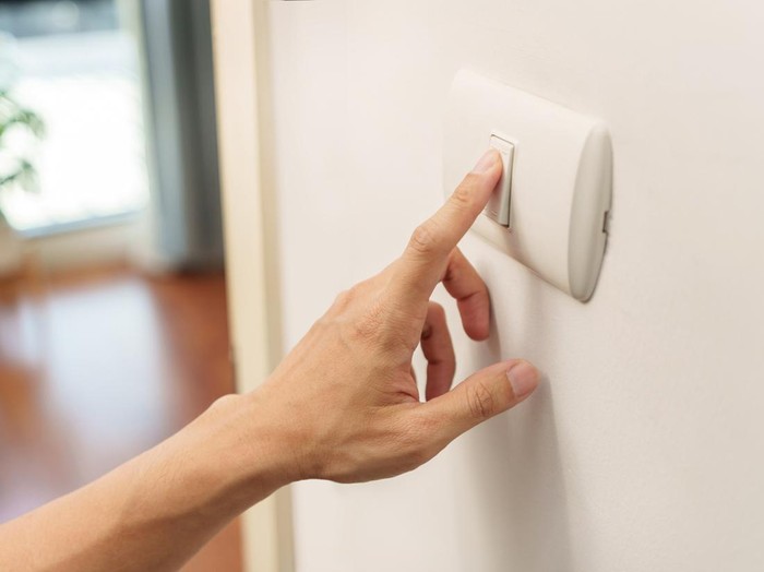 Closeup of finger is turning off on lighting switch on white wall at home. Power, Energy, Saving Electrical, Copy space.