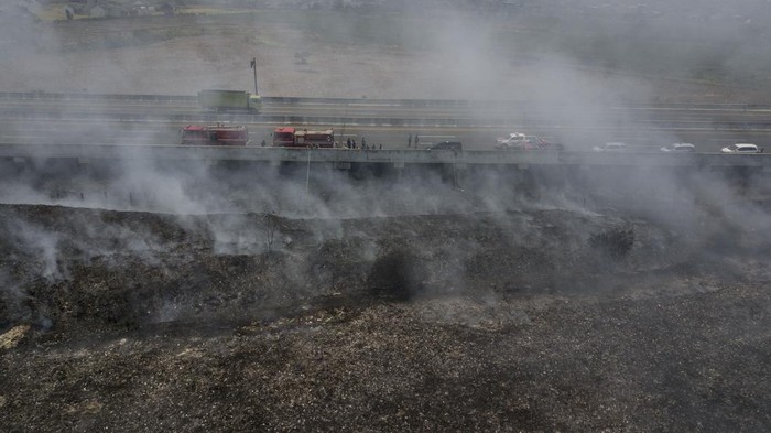 Seorang petugas pemadam kebakaran melintas diantara asap sisa kebakaran TPS (Tempat Pembuangan Sampah) ilegal samping Tol Cibitung-Cilincing, Desa Sumber Jaya, Tambun Utara, Kabupaten Bekasi, Jawa Barat, Senin (25/9/2023). Sebanyak 17 unit mobil memadamkan api secara bergantian selama tiga hari karena asap sisa kebakaran masih menutupi jarak pandang kendaraan yang melintas di tol dan terdapat jalur pipa gas di lokasi kebakaran.  ANTARA FOTO/ Fakhri Hermansyah/aww.