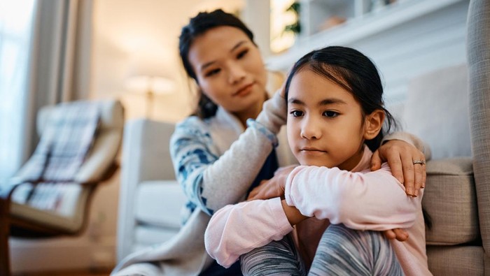 Sad Asian girl being consoled by her mother at home.