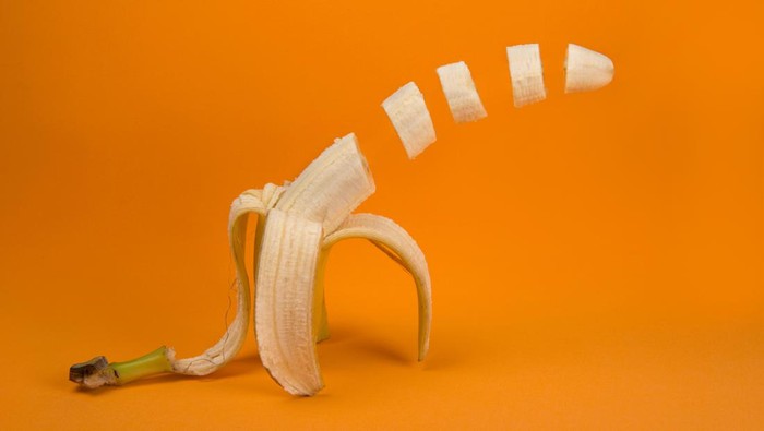 A peeled and sliced single banana isolated on a natural colored background.