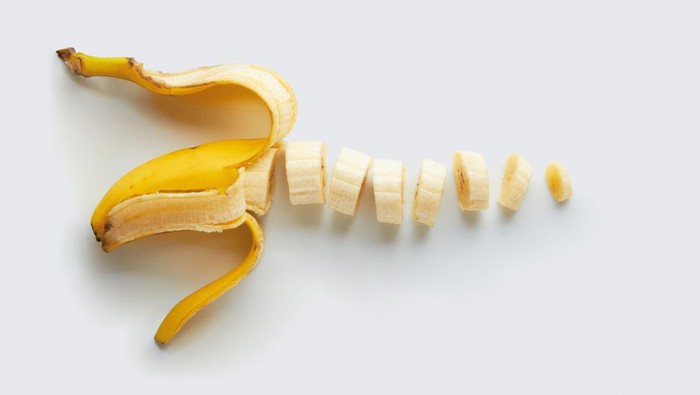 A peeled and sliced single banana isolated on a natural colored background.