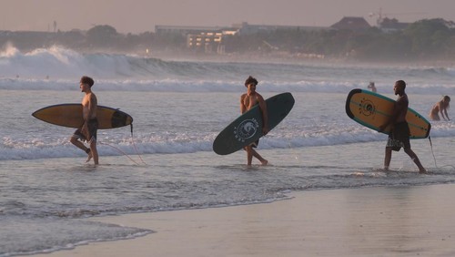 Sejumlah wisatawan membawa papan selancar berjalan menuju ke tengah laut saat berlibur di Pantai Kuta, Badung, Bali, Senin (25/9/2023). Kepala Dinas Pariwisata Provinsi Bali Tjok Bagus Pemayun mengatakan untuk retribusi sebesar Rp150 ribu kepada turis asing yang masuk Pulau Dewata diterapkan mulai Februari 2024 dan mekanismenya serta tata cara pungutan uang kepada turis asing hingga saat ini masih disusun dalam Peraturan Gubernur (Pergub) Bali. ANTARA FOTO/Nyoman Hendra Wibowo/aww.
