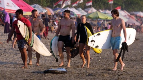 Sejumlah wisatawan membawa papan selancar berjalan menuju ke tengah laut saat berlibur di Pantai Kuta, Badung, Bali, Senin (25/9/2023). Kepala Dinas Pariwisata Provinsi Bali Tjok Bagus Pemayun mengatakan untuk retribusi sebesar Rp150 ribu kepada turis asing yang masuk Pulau Dewata diterapkan mulai Februari 2024 dan mekanismenya serta tata cara pungutan uang kepada turis asing hingga saat ini masih disusun dalam Peraturan Gubernur (Pergub) Bali. ANTARA FOTO/Nyoman Hendra Wibowo/aww.