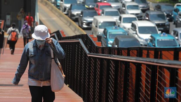 Pejalan kaki menggunakan payung untuk menghindari terik matahari di kawasan Jembatan Pinisi di halte busway Karet, Jakarta, Rabu (27/9/2023). (CNBC Indonesia/Muhammad Sabki)