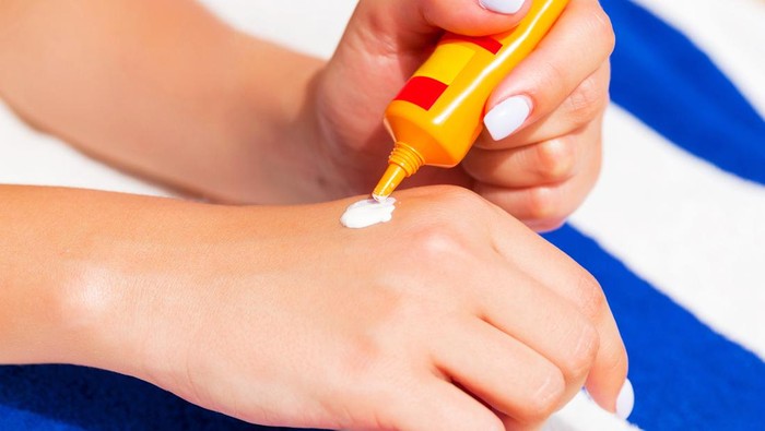 Woman hands putting sunscreen from a suncream bottle.
