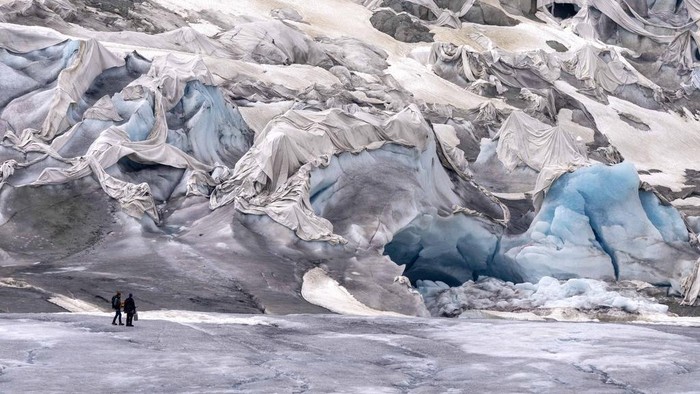 Darurat! Gletser di Swiss Hilang 10 Persen dalam Dua Tahun FILE - A team member of Swiss Federal Institute of Technology glaciologist and head of the Swiss measurement network 'Glamos', Matthias Huss, passes the Rhone Glacier covered by sheets near Goms, Switzerland, on June 16, 2023. A Swiss Academy of Sciences panel is reporting a dramatic acceleration of glacier melt in the Alpine country, which has lost 10% of its ice volume in just two years after high summer heat and low snow volumes in winter. (AP Photo/Matthias Schrader, File)