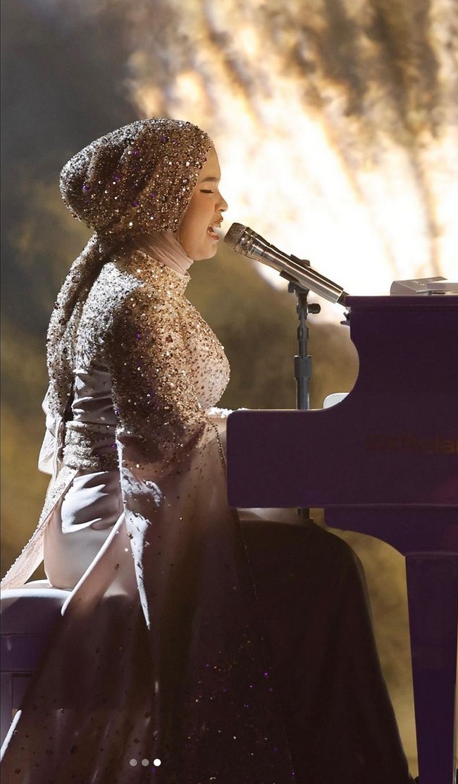 Saat yang ditunggu-tunggu akhirnya tiba. Tiga bulan sejak tampil di audisi, Putri tampil di semifinal America’s Got Talent 2023. Menyanyi sambil main piano, ia bergaya ekstra glamor mengenakan gaun nuansa emas berkilau, juga dari koleksi Tiffany Liem. Foto: Instagram/@arianinismaputri