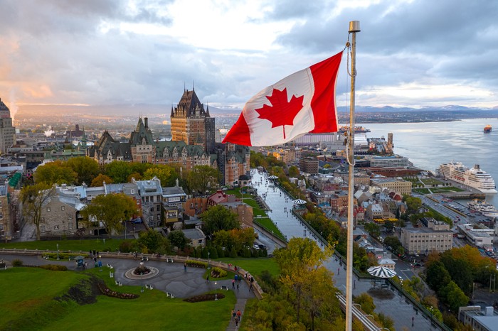 A flowing Canadian flag on a flagpole. Taken at sunset with Old Quebec City and the St. Lawrence River in the background. Aerial HDR view.