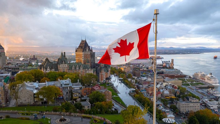 A flowing Canadian flag on a flagpole. Taken at sunset with Old Quebec City and the St. Lawrence River in the background. Aerial HDR view.
