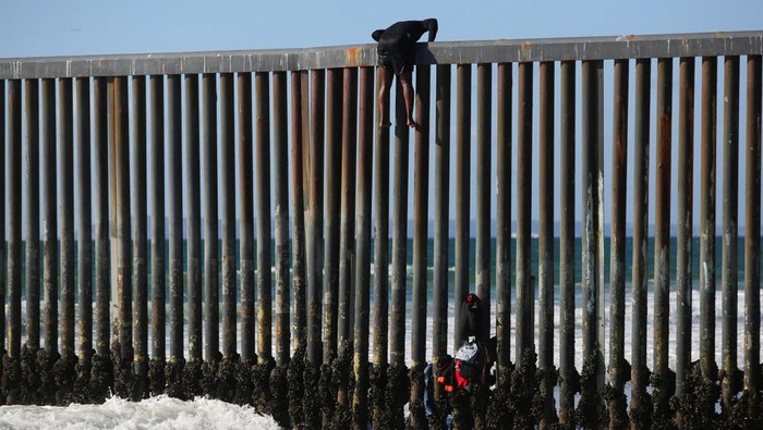 A migrant climbs the border fence to cross into the U.S. to request asylum, at Playas de Tijuana, in Tijuana, Mexico October 2, 2023. REUTERS/Jorge Duenes