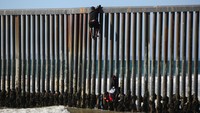 Seorang migran memanjat pagar perbatasan di Playas de Tijuana, Tijuana, Meksiko, Selasa (2/10/2023).