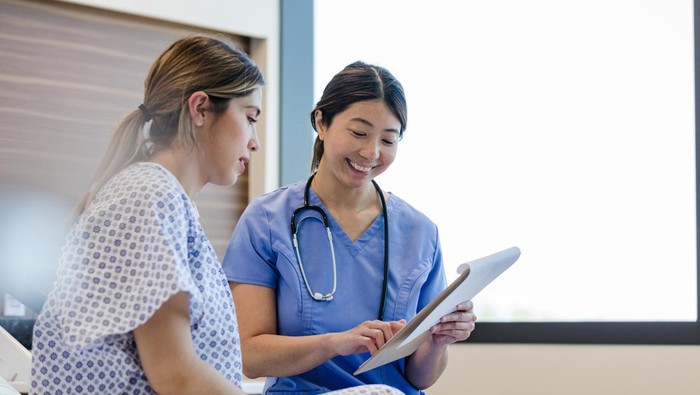 At the hospital, the mid adult female doctor gives her young adult female patient the good news from her medical tests.