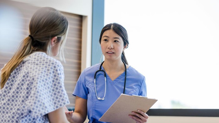 At the hospital, the mid adult female doctor gives her young adult female patient the good news from her medical tests.
