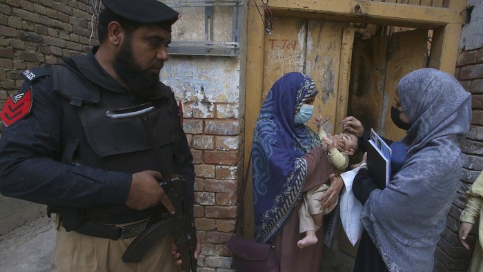 A police officer stands guard as a health worker administers a polio vaccine to a child at a neighborhood of Peshawar, Pakistan, Monday, Oct. 2, 2023. (AP Photo/Muhammad Sajjad)