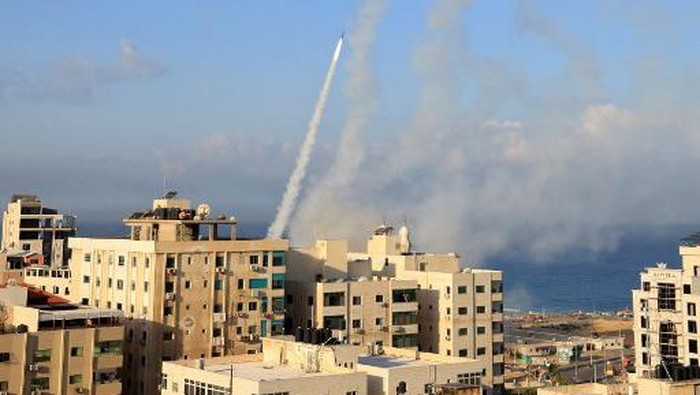 EDITORS NOTE: Graphic content / People standing on a rooftop watch as a ball of fire and smoke rises above a building in Gaza City on October 7, 2023 during an Israeli air strike. At least 70 people were reported killed in Israel, while Gaza authorities released a death toll of 198 in the bloodiest escalation in the wider conflict since May 2021, with hundreds more wounded on both sides. (Photo by MAHMUD HAMS / AFP)