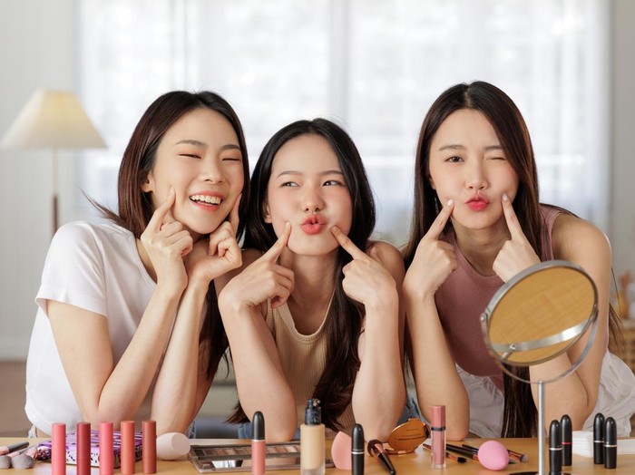 Close up of a youthful female model applying moisturizer to her face. Young korean woman putting moisturizer cream on her pretty face against pink background.