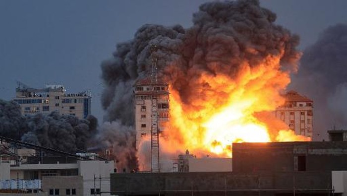 EDITORS NOTE: Graphic content / People standing on a rooftop watch as a ball of fire and smoke rises above a building in Gaza City on October 7, 2023 during an Israeli air strike that hit the Palestine Tower building. At least 70 people were reported killed in Israel, while Gaza authorities released a death toll of 198 in the bloodiest escalation in the wider conflict since May 2021, with hundreds more wounded on both sides. (Photo by MAHMUD HAMS / AFP)