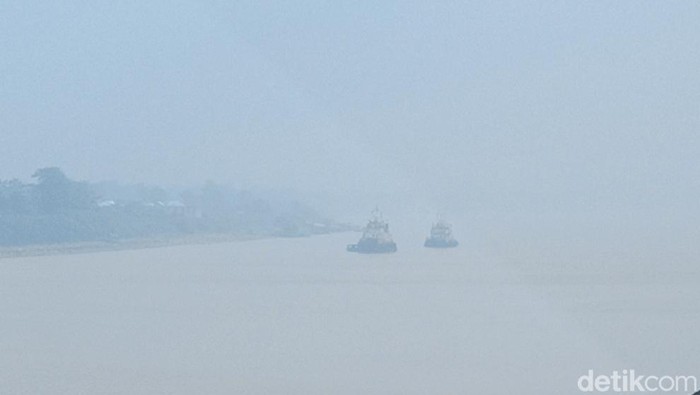 Terlihat dari kejauhan dua kapal berada di tengah jalur sungai Batanghari Jambi saat diselimuti kabut asap
