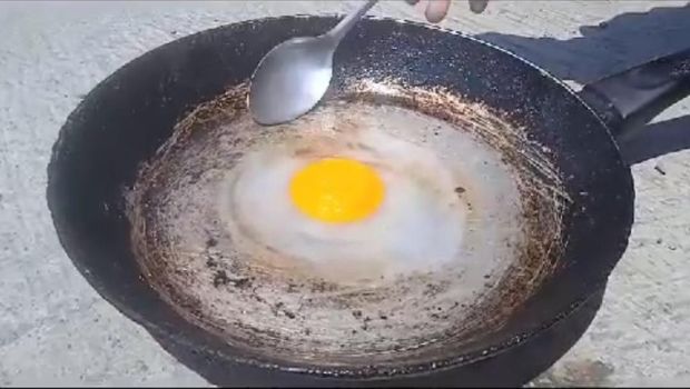 Seorang bocah bereksperimen menggoreng telur di bawah terik matahari.