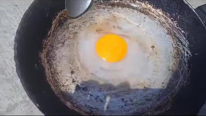 Seorang bocah bereksperimen menggoreng telur di bawah terik matahari.