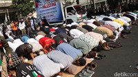 Massa menggelar terpal dan melaksanakan salat di sekitar mobil komando.  