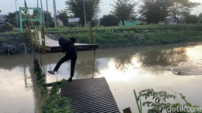 Seorang warga setempat mencoba menyeberang menggunakan jembatan Titi Bambu yang putus. (Kartika Sari/detikSumut)