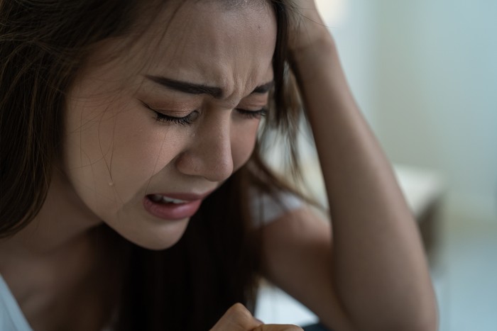 Asian beautiful depression girl crying in tears sit on bed in bedroom. Attractive unhappy young woman feeling sad lonely and upset with life problem and hold tissue on hands in dark night room at home
