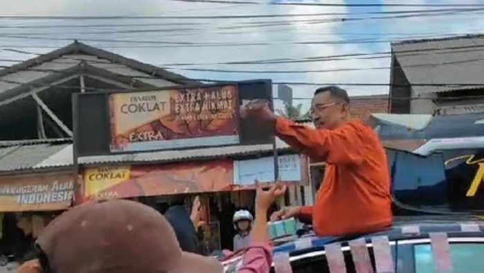 Endang Suhendar membagikan uang kepada masyarakat dari atas mobil di jalan raya, Pandeglang, Banten.