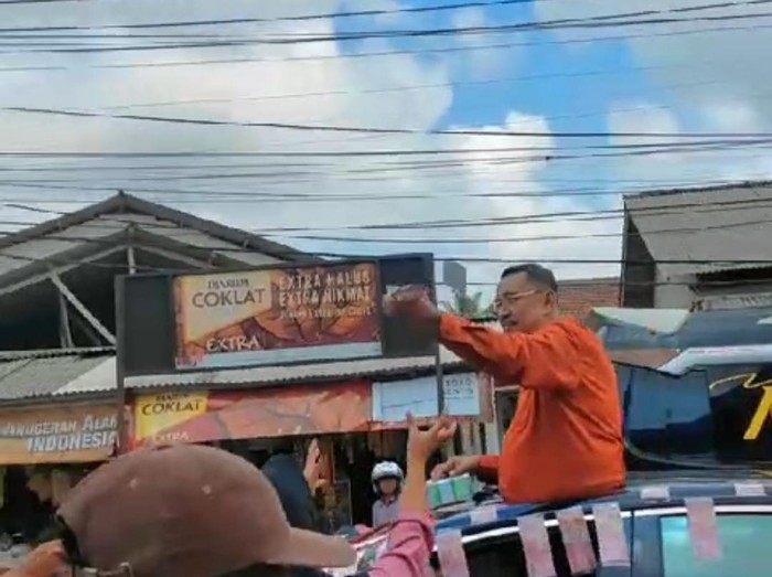 Endang Suhendar membagikan uang kepada masyarakat dari atas mobil di jalan raya, Pandeglang, Banten.