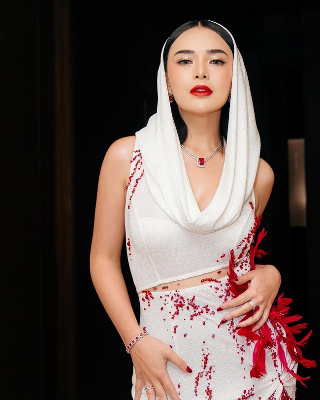 Dress putih panjang tanpa lengan itu memiliki aksen rumbai pada bagian belahan di area pahanya. Di salah satu sisinya juga terdapat aksen seperti bulu-bulu dan batu-batu berwarna merah. Diketahui bahwa gaun unik yang dikenakan Amanda itu merupakan rancangan dari desainer Yenty Tan. Foto: Instagram