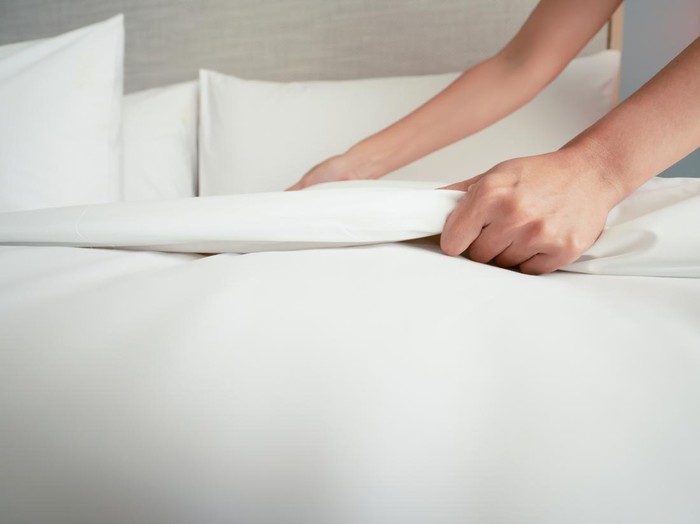Female Hand set up white bed sheet in room hotel.