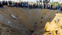 Warga berkerumun di sekitar kawah bekas hantaman rudal Israel di Khan Younis, Jalur Gaza.  
