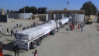 Relawan Mesir bersorak dan mengibarkan bendera saat truk pengangkut bantuan yang ditempatkan di perbatasan Rafah dan Gaza di sisi Mesir melewati penyeberangan pada Sabtu pagi (21/10/2023). (AP Photo/Mohammed Asad)