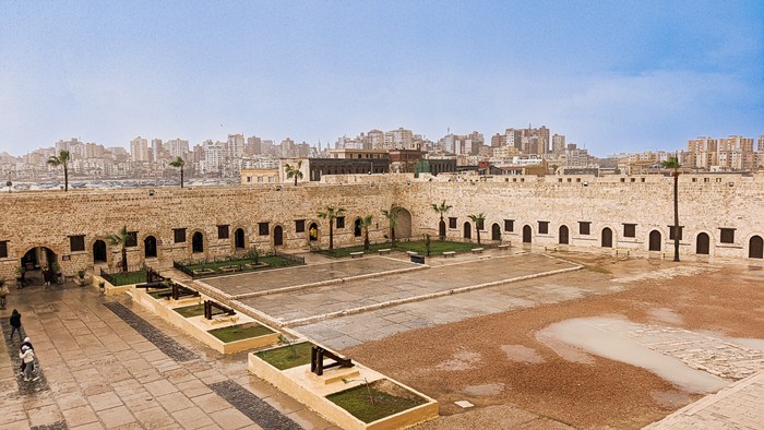 Wide angle photo inside the Qaitbay Citadel of Alexandria Egypt during winter after rain fall. This fort has been standing strong since the 15th century. Behind the citadel, we can see the beautiful Alexandrian cityscape clearly with cloudy blue sky.