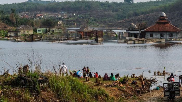 Pengunjung berswafoto dengan latar belakang kampung yang mulai tenggelam di Kampung Sinday, Lebak, Banten, Minggu (22/10/2023). Kampung tenggelam yang dijadikan genangan air untuk menampung bendungan Karian tersebut menjadi objek wisata dadakan bagi masyarakat setempat yang ingin melihat kondisi kampung itu. ANTARA FOTO/Muhammad Bagus Khoirunas/nz