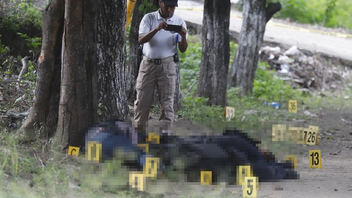 A police officer from the Attorney Generals Office takes photographs of the bodies of slain police officers in El Papayo, Coyuca de Benitez municipality, Guerrero state, Mexico, Monday, Oct. 23, 2023. Twelve police officers and their boss were gunned down on Monday, according to Guerrero state prosecutor's office. (AP Photo/Bernardino Hernandez)