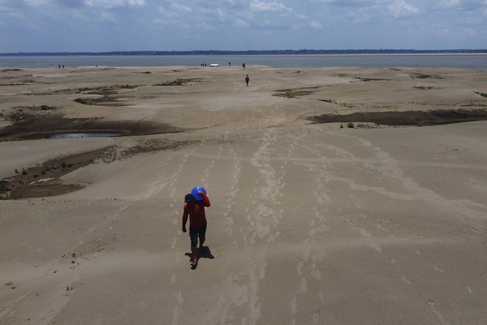 Residents of a riverside community carry food and containers of drinking water after being distributed by the states humanitarian aid action due to the ongoing drought and high temperatures that affect the region of the Solimoes River, in Careiro da Varzea, Amazonas state, Brazil, Tuesday, Oct. 24, 2023. (AP Photo /Edmar Barros)