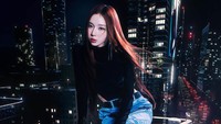 Winter tampil dengan rambut panjang di foto ini, duduk di sebuah gedung dengan baliho LED di sekitarnya. (Foto: dok. SM Entertainment)