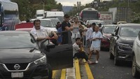 Sebagian orang menunggu di luar mobil sembari menunggu petugas yang membersihkan jalan yang diakibatkan oleh Badai Otis.