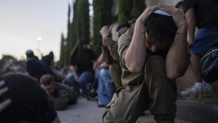 Israel Kumandangkan Sirene Peringatan Rudal, Warga Ketakutan Israelis take cover as a siren warns of incoming rockets fired from the Gaza Strip, during the funeral of the Israeli man Sagiv Ben Svi, killed by Hamas militants while attending a music festival, at a cemetery in Holon, central Israel, Thursday, Oct. 26, 2023. More than 1,400 people were killed and over 200 taken captive in an multi-front attack by the militant group that rules Gaza on Oct. 7.(AP Photo/Petros Giannakouris)