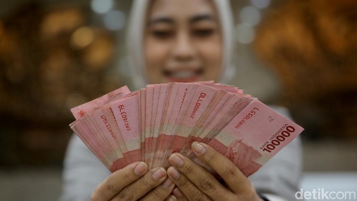 Teller bank menghitung uang Dollar diatas tumpukan Rupiah.