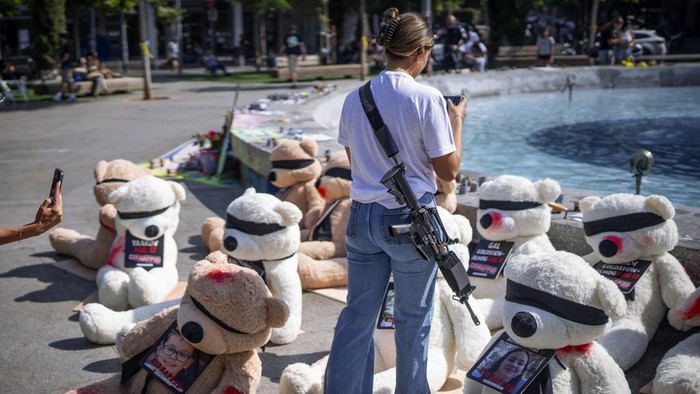 Potret Tentara Israel Tenteng Senjata Meski Tidak Bertugas An off-duty Israeli soldier takes photos of an installation of blindfolded giant teddy bears adorned with photos of Israelis held captive in Gaza, in Tel Aviv, Israel, Wednesday, Oct. 25, 2023. The installation is meant to draw attention to over 200 people who were abducted by Hamas militants during a bloody and unprecedented Oct. 7 cross-border attack. (AP Photo/Oded Balilty)