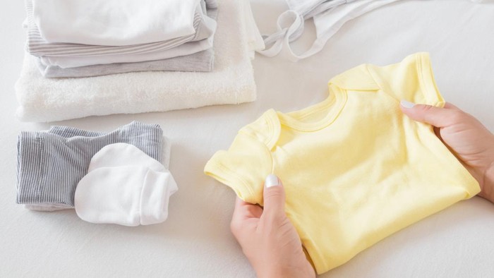 Womans hands sorting new baby clothes on white bed sheet. Mothers daily duties. Soft colors. Closeup.