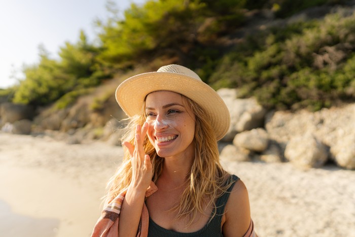 Photo of a young woman applying sunscreen on her face.