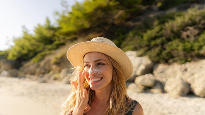Photo of a young woman applying sunscreen on her face.