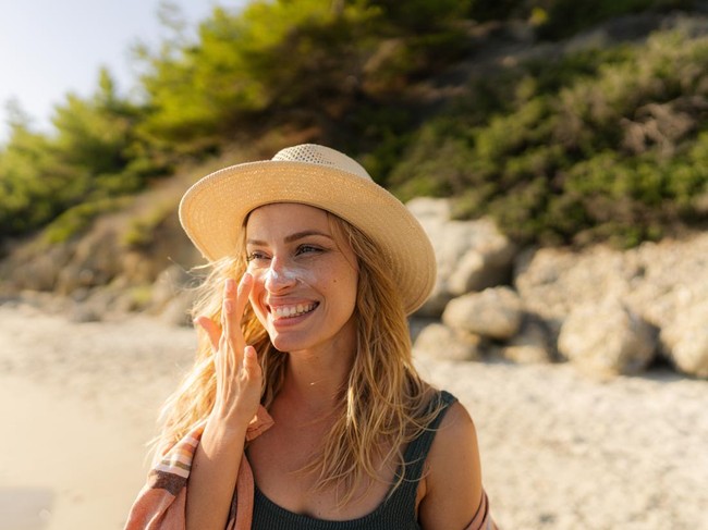 1458599573. Photo of a young woman applying sunscreen on her face.