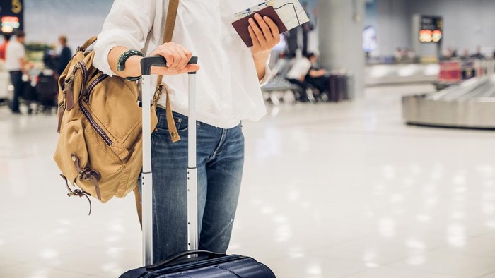 Woman backpacker holding passport and map with suitcase standing at check in baggage at airport terminal,traveler concept.