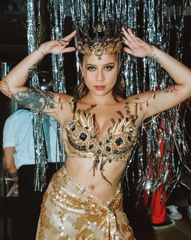 Tampilan selanjutnya Awkarin memilih cosplay menjadi Ratu Pantai Utara. Selebgram 25 tahun itu tampil seksi dalam balutan busana berwarna gold. Penampilannya itu juga dilengkapi dengan mahkota berwarna senada di kepalanya. Foto: Instagram