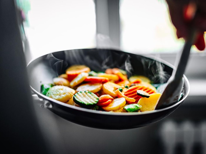 Woman cooking tasty vegetable mix stew in pan on kitchen.