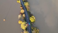 Sebuah jalan raya terlihat dikepung banjir saat sebuah mobil melintas.